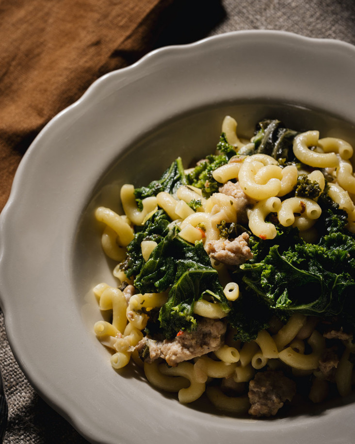 Un bol de macaroni avec chair de saucisse émiettée, du kale et des haricots cannellini.